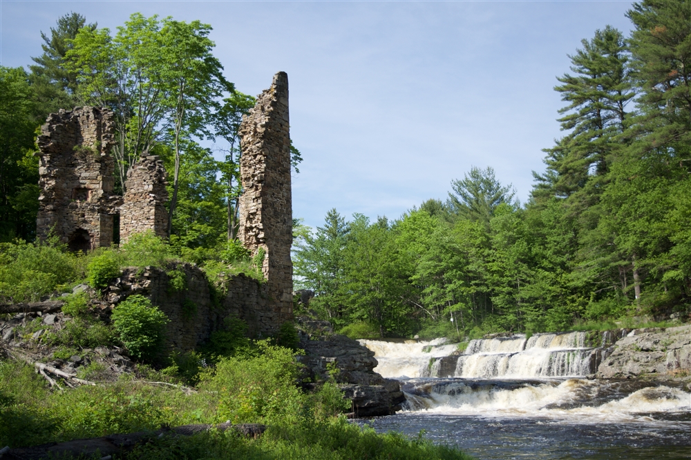 Triple-tier waterfall in the middle of a lush green forest with large stone pillars on the left side