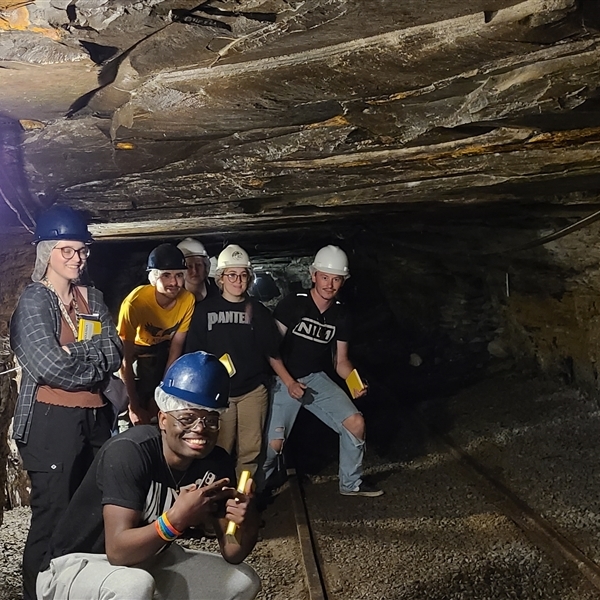 Six students wearing hardhats smiling in a mine