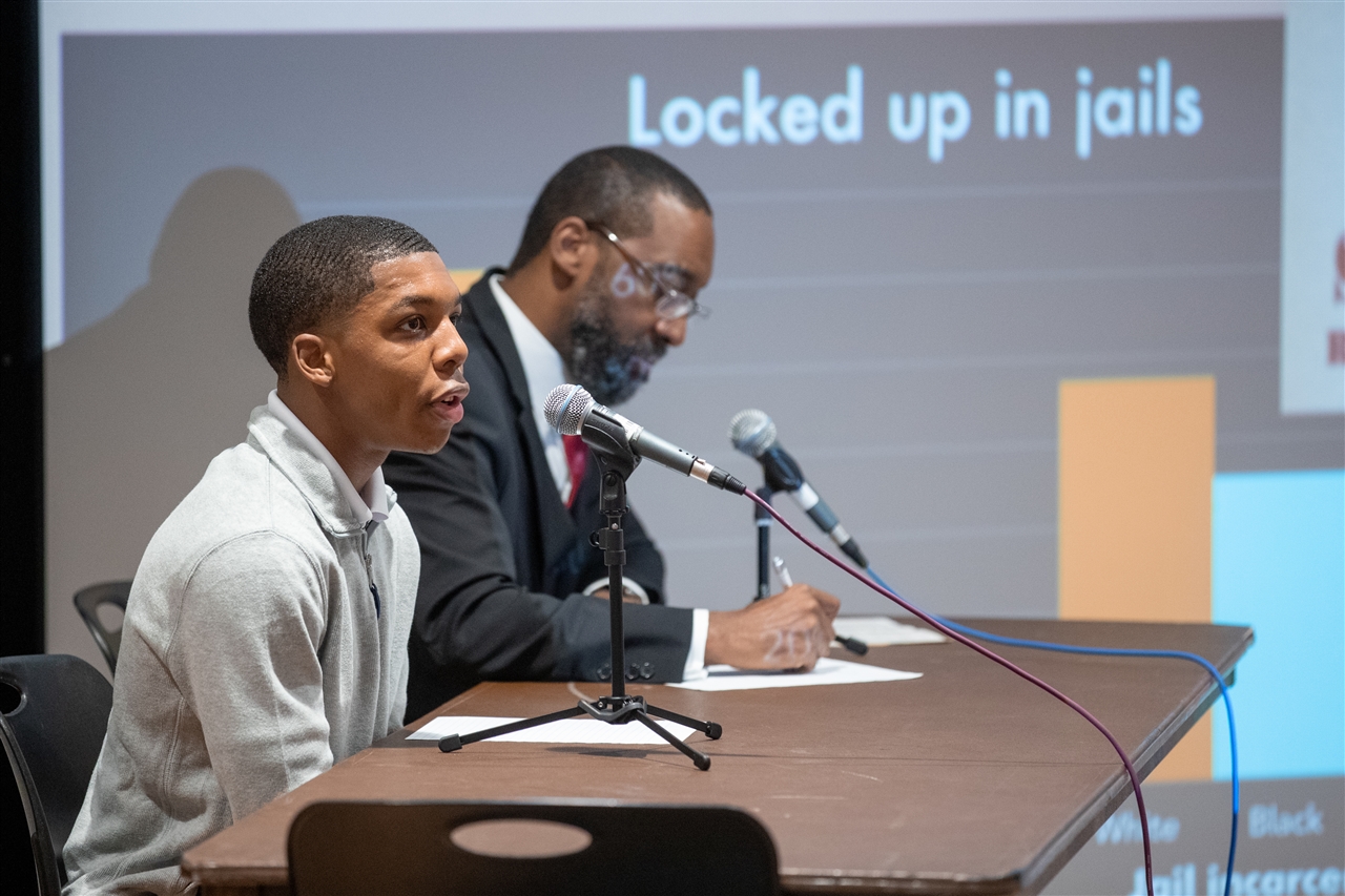 Two male speakers presenting in the MSU in front of a powerpoint slide that says "locked up in jails"