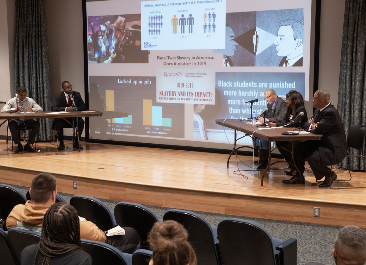 Distance shot of both panels at the slavery and its impact conference, presenting a powerpoint slide titled "slavery in America: does it matter in 2019?"