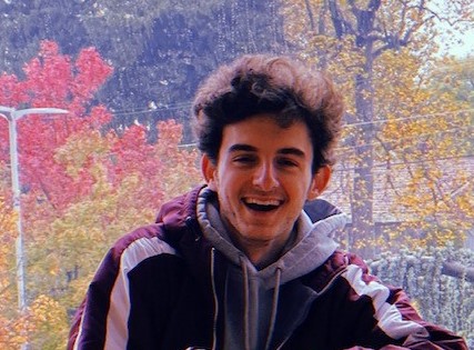 Evan Santos smiling widely in front of a streetview painting with autumn trees