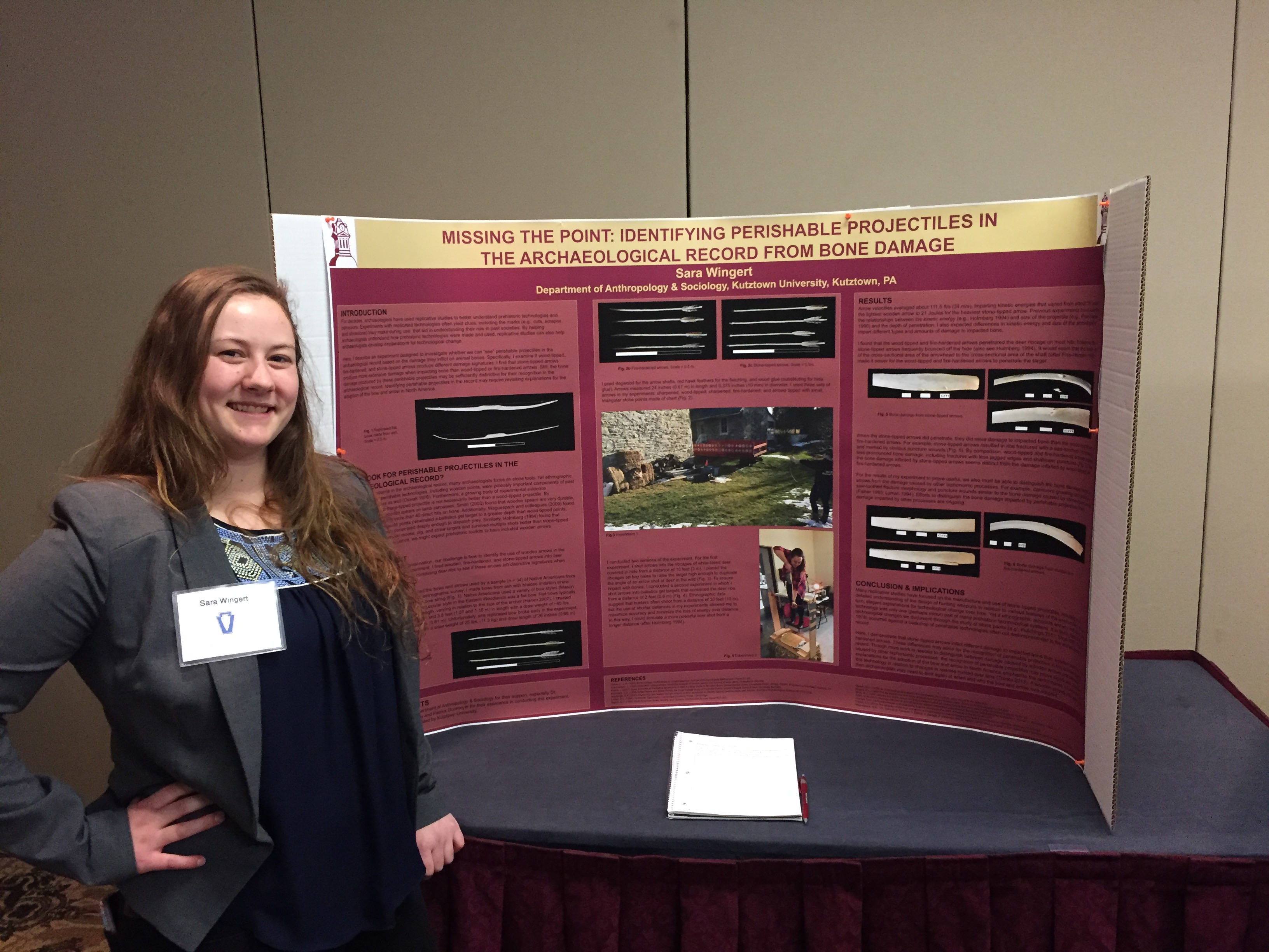 Female student smiling and standing next to her presentation poster on "Missing the Point: Identifying  perishable projectiles in the archaeological record from bone damage."