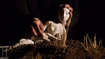 A pair of hands positioning pieces of a papier-mâché doll on a bed of hay 