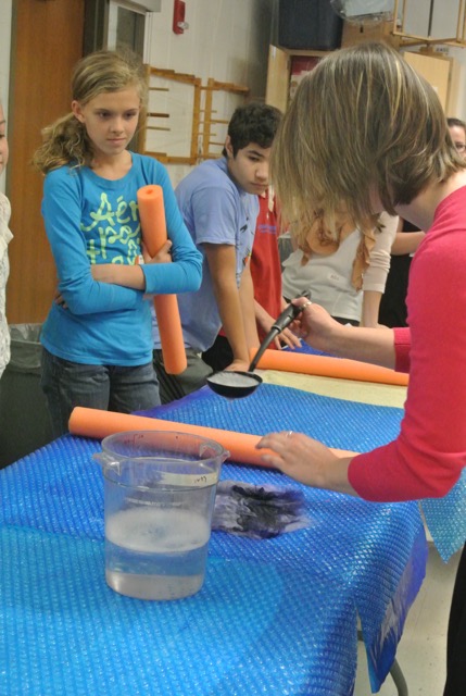 elementary schoolers watching a demonstration at a craft table 