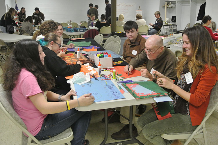 Participants of varying ages creating posters at a table and smiling