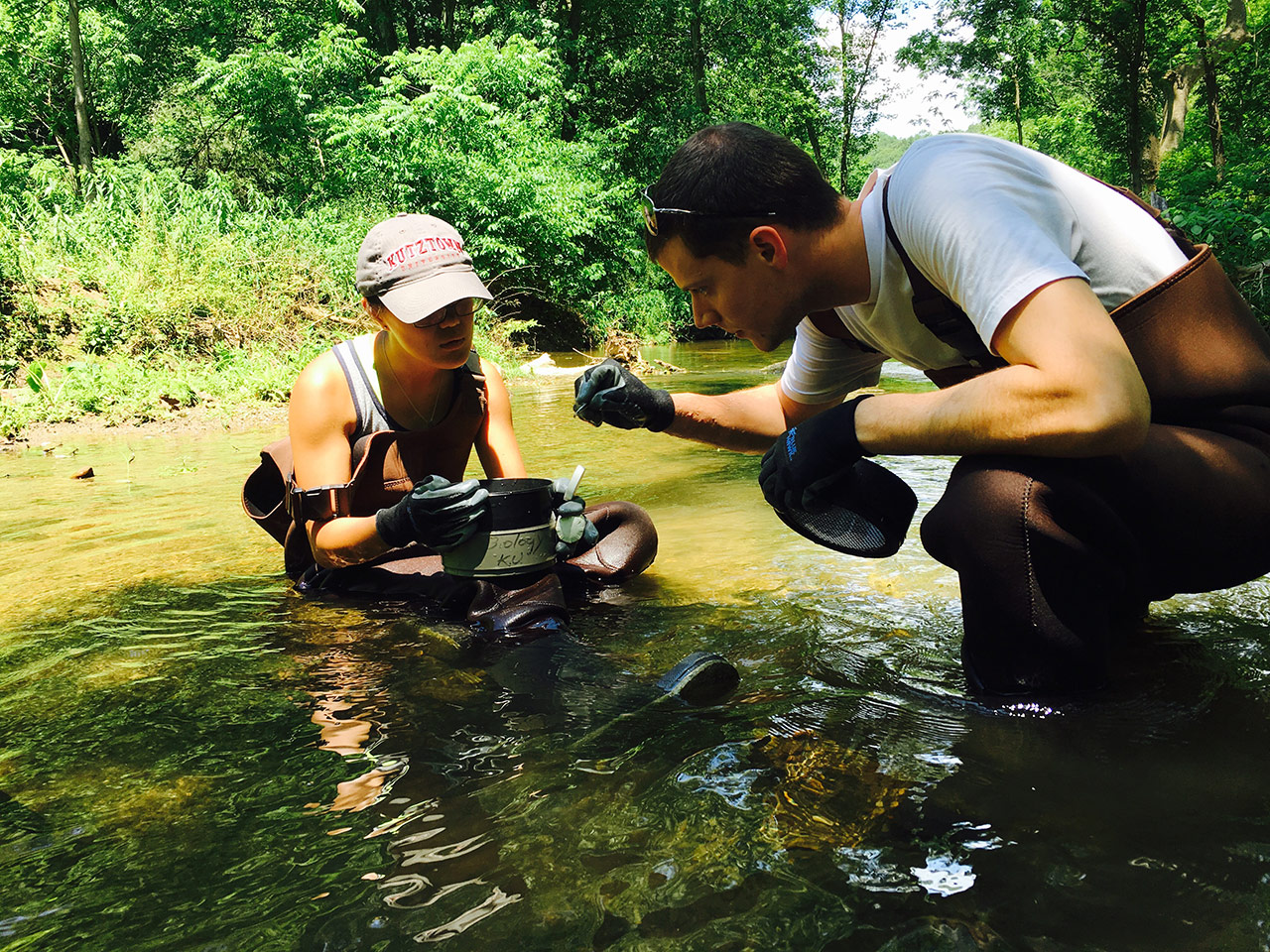 Two students crouching in a river and examining the specimen they collected