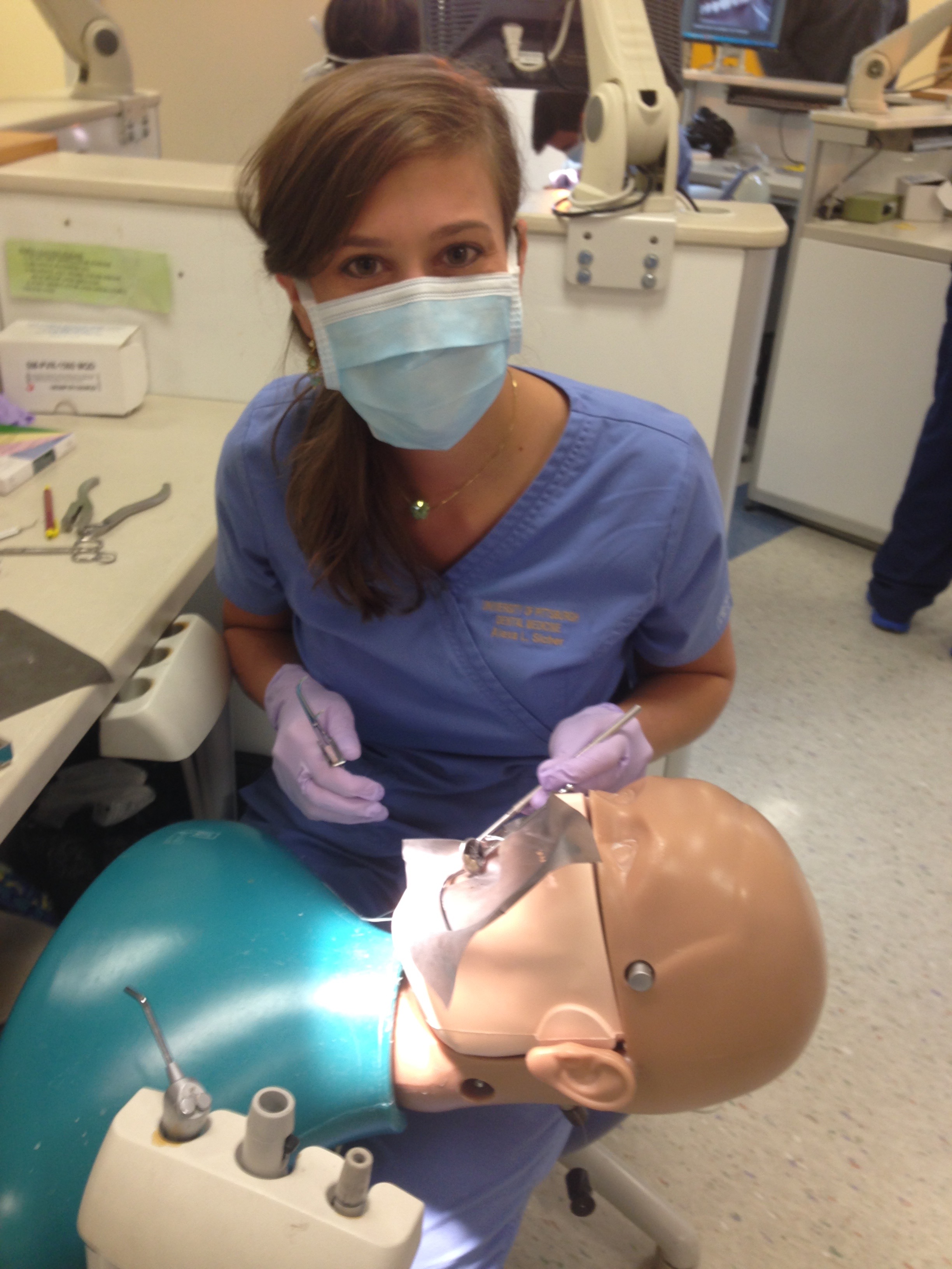 Female student in scrubs performing a practice operation on the face of a dummy.