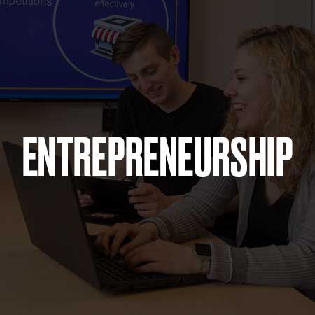 A male and female working together at a table with laptops and the word entrepreneurship over it