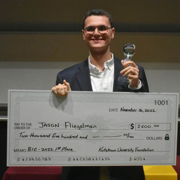 Jason Fliegelman, first place winner of the 2022 business idea competition, holding a large check for $2,500 and a lightbulb trophy