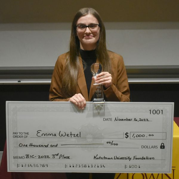 Emma Wetzel, third place winner, holding up a large check for $1000 and a lightbulb trophy