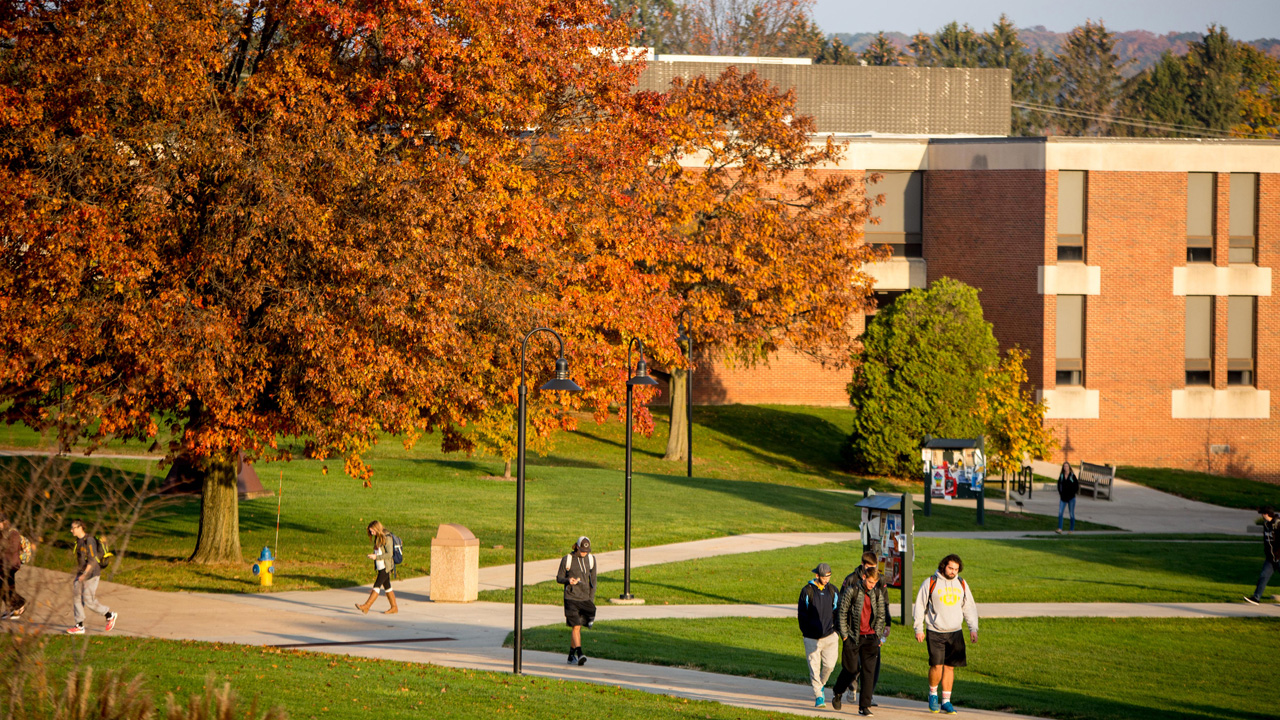Kutztown University's campus with autumn leaves and students walking along the paths in the foreground.