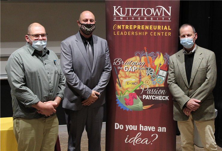 Josh Kovitch, John Stetler, and John Dever standing in front of the Business Idea Competition sign