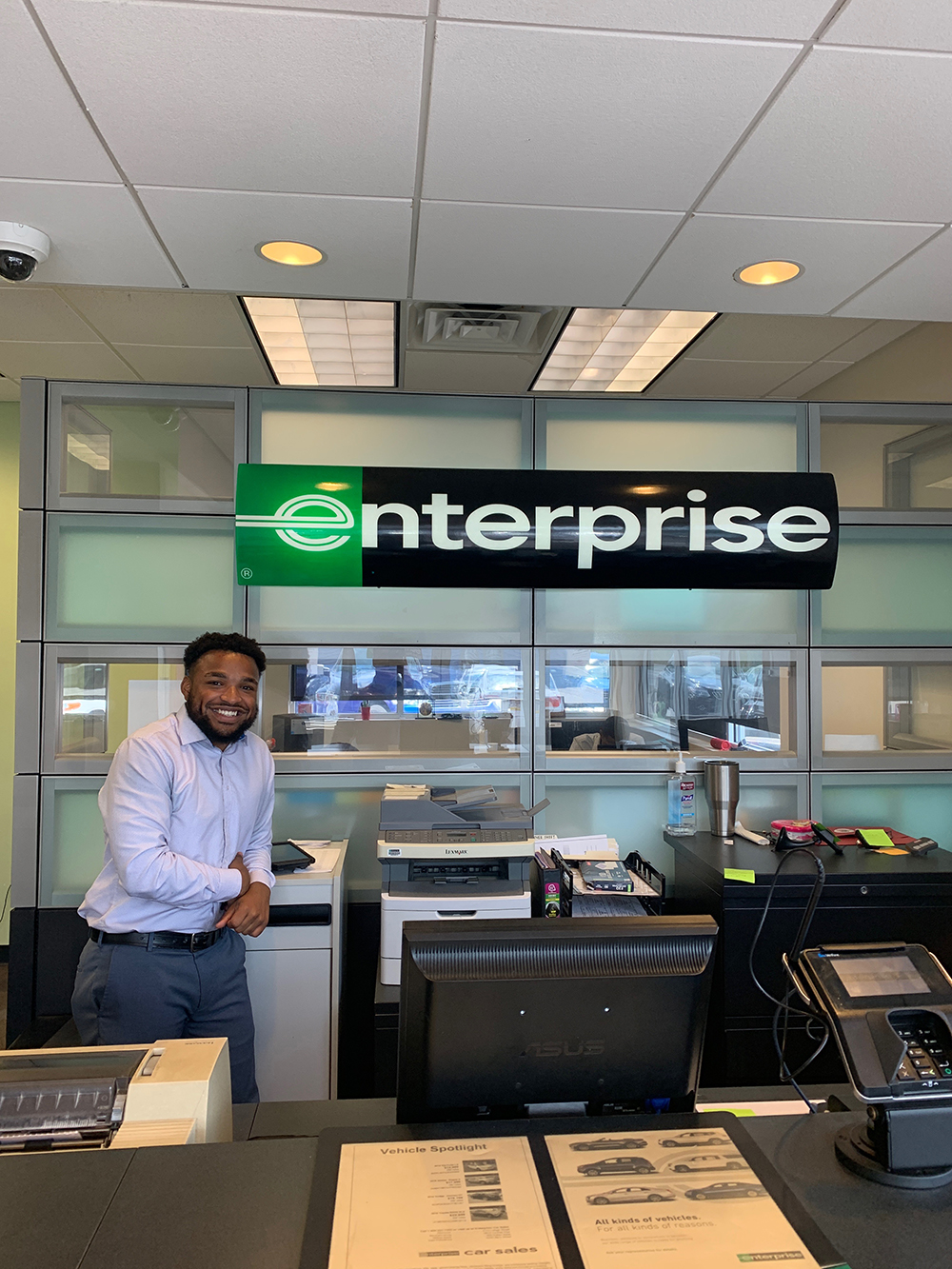 Felix Alberto, leaning on a copy machine and smiling under an enterprise sign at his internship