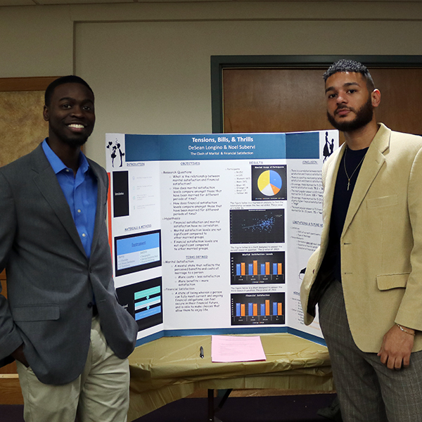 Students standing on either side in front of a poster presentation on "tension, bills and thrills"