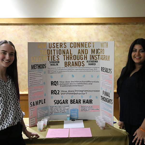 Two students standing on either side in front of a poster presentation titled "how students connect with traditional and micro-celebrities through Instagram brands" 