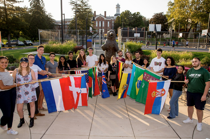 students in triangle formation holding international flags outside