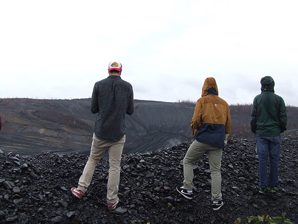 students standing on a waste coal pile and examining a large crater beneath them