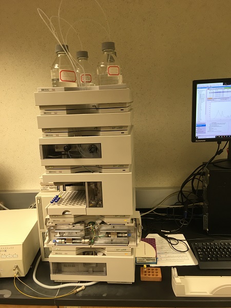 multiple gray instrument boxes in a stack with solvent bottles on top beside a computer station