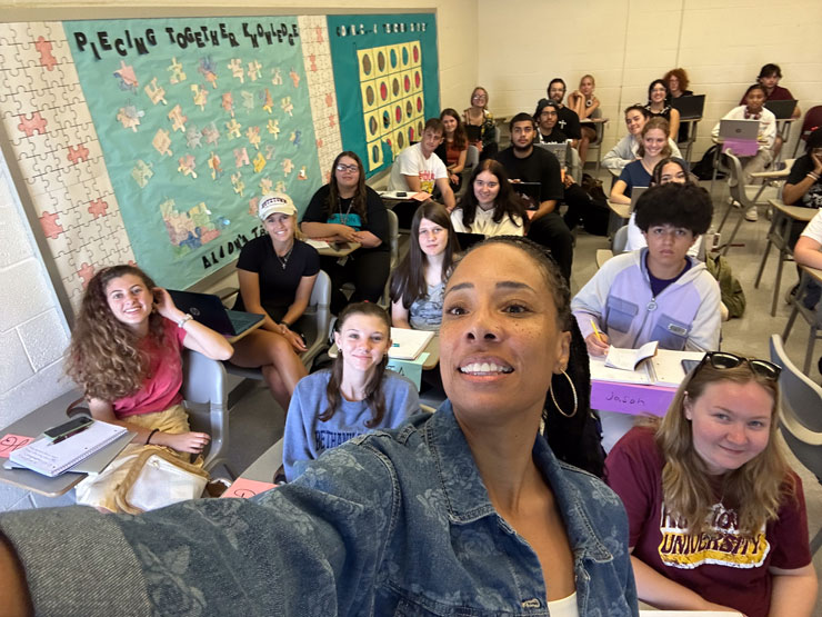 Amber Pabon takes a selfie photo with students in the background in Dr. Muzeta's First-year Seminar class.