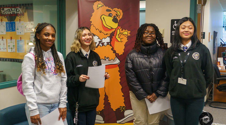 Students pose for a picture in front of an Avalanche the Golden Bear cartoon poster.