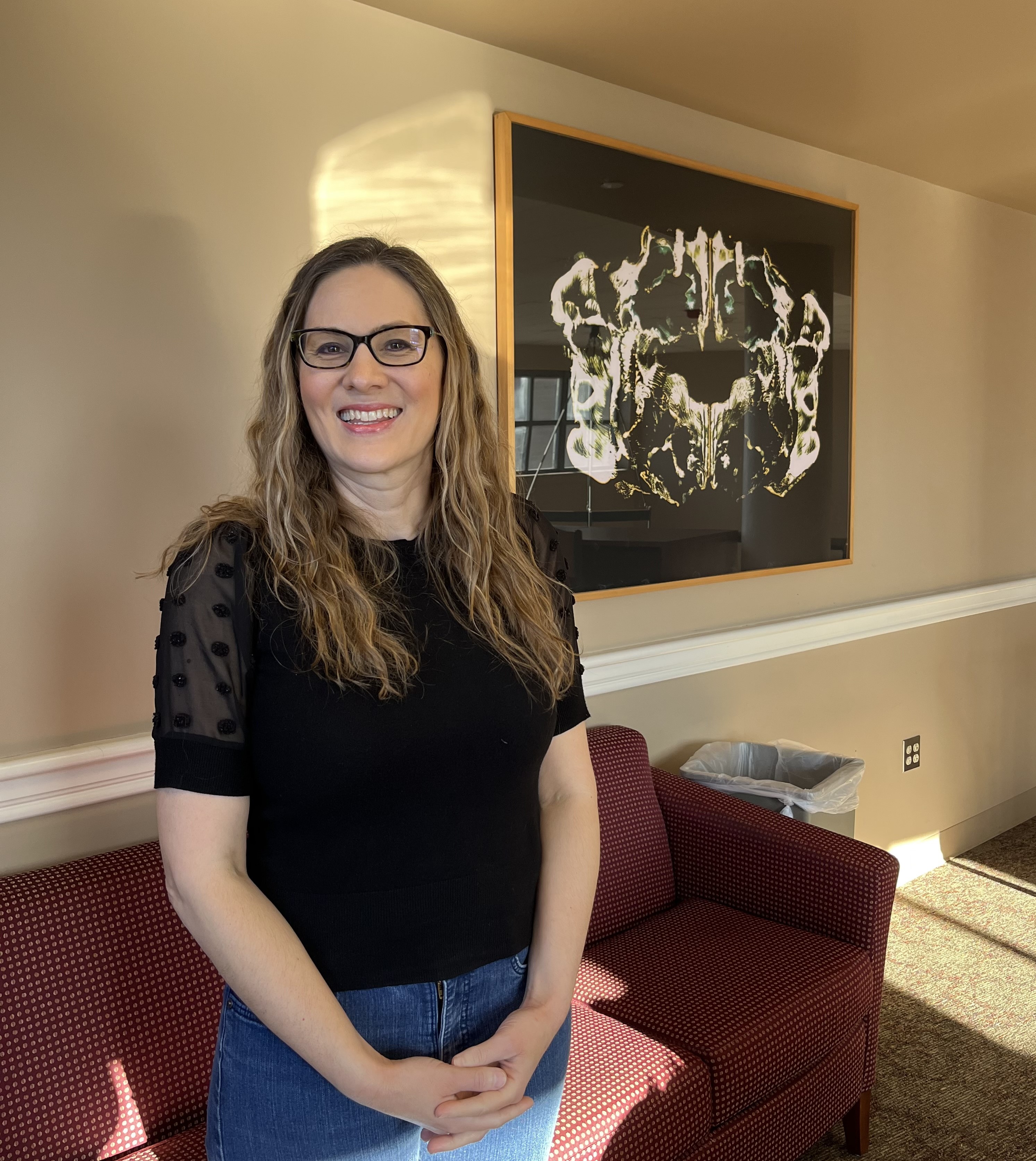 Dr. Jennifer Topale stands in the left center of the frame, with art work and a red couch behind her.