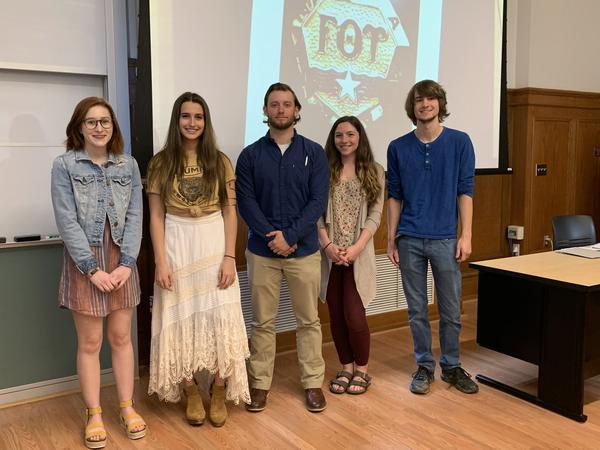 2019 GTU Initiates standing in a group and smiling in front of a slide show with the insignia 