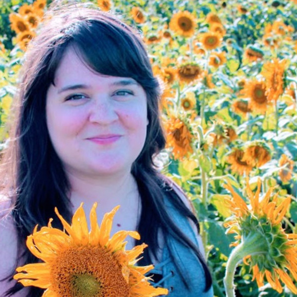 headshot of Corey holding a sunflower, with a field of sunflowers in the background