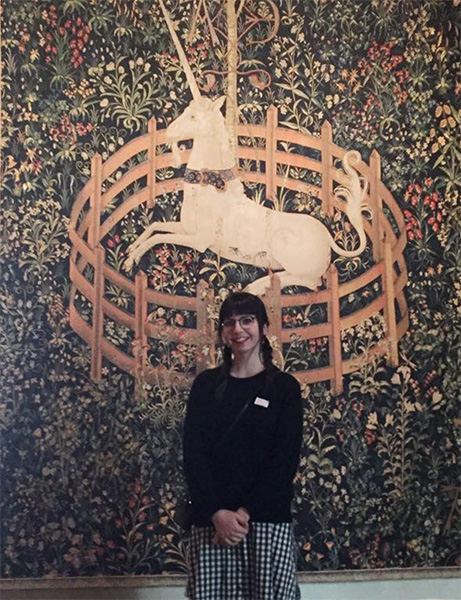 Liz Hopkins standing in front of a tapestry with a deer in a pen 
