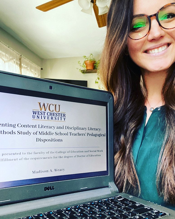 Madison Weary smiling next to her laptop, which displays her dissertation title page