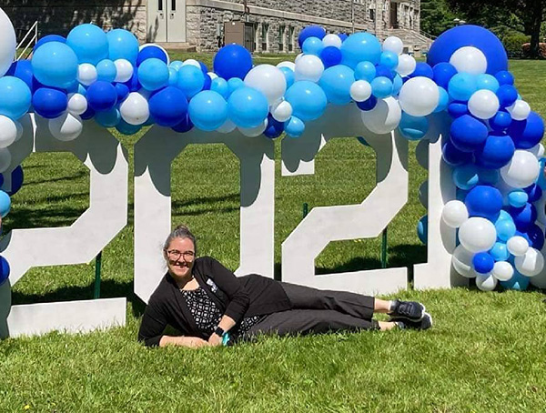 Tarra reclining on ground in front of large 3D 2021 sign, draped in blue and white balloons 