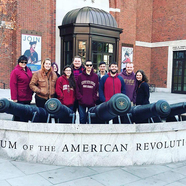 Dr Derr and students standing behind sign at Museum of the American Revolution