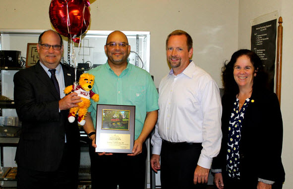 Thomas Robinson holding his employee of the month award, surrounded by members of the HR council, with Dr. Hawkinson holding the celebratory balloons and stuffed bear  