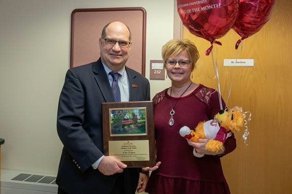 Kim Kilgus holding her stuffed bear and balloons as Dr. Hawkinson presents her with the employee of the month placard 