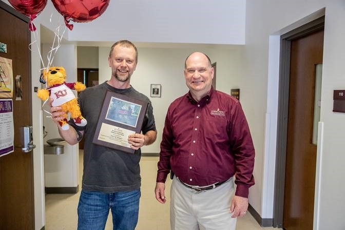 David Boyer holding his employee of the month placard, stuffed Avalanche bear, and balloons next to Dr. Hawkinson 