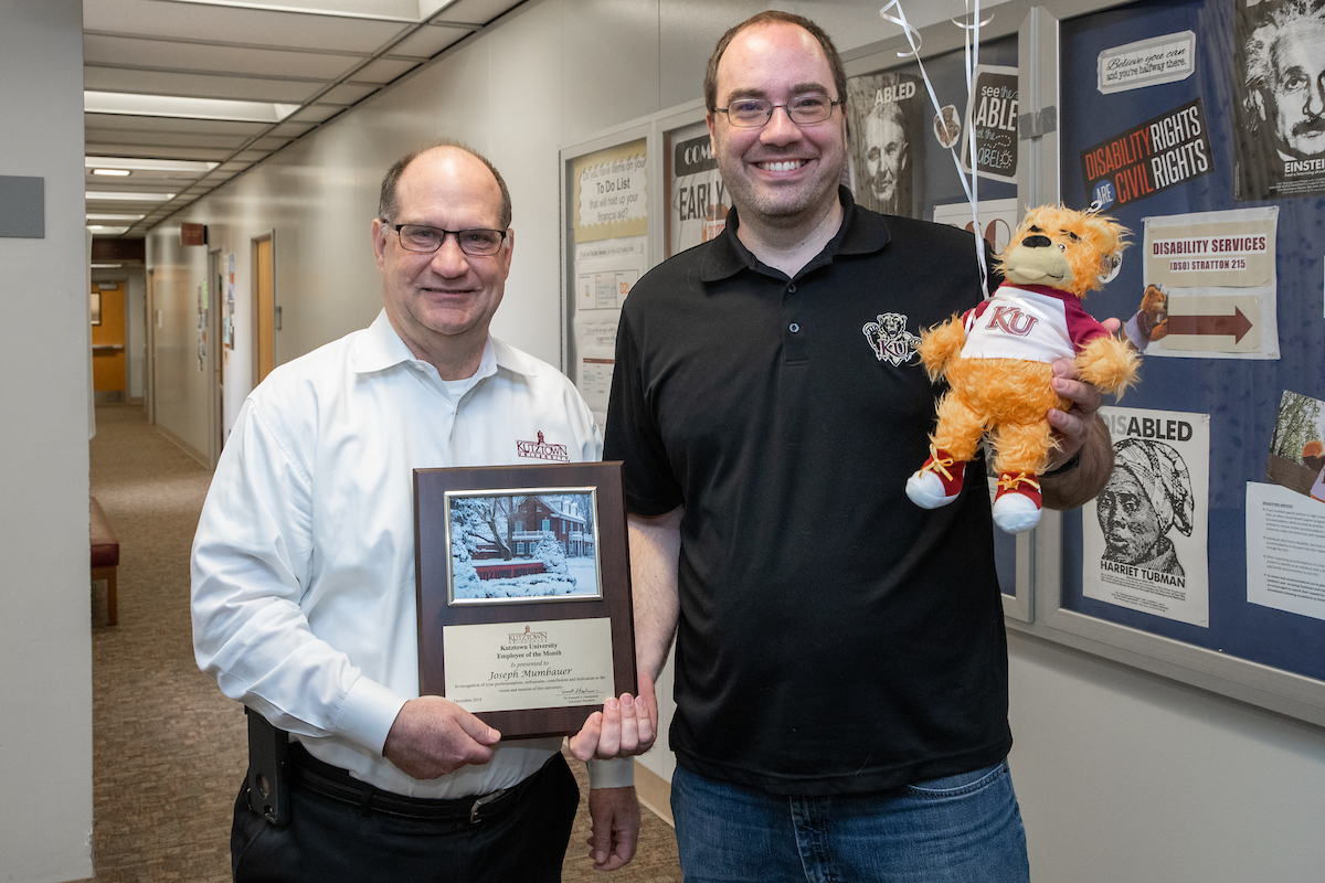Joe Mumbauer holding his stuffed golden bear gift while President Hawkinson holds up the Employee of the Month placard 