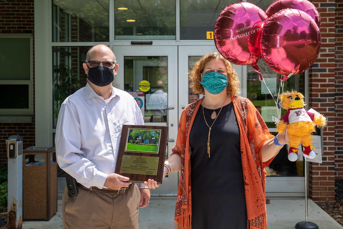 Jennifer Weidman holding her balloons and stuffed bear while President Hawkinson presents her with the Employee of the Month placard 