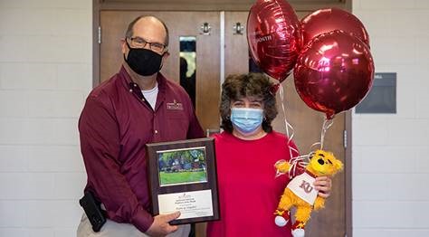 Nancy Snyder and President Hawkinson holding the Employee of the Month placard between them, while Snyder holds balloons and a stuffed bear in her other hand