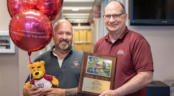 Louis Rivera holding celebratory balloons and a stuffed golden bear while President Hawkinson hands him the Employee of the Month award 