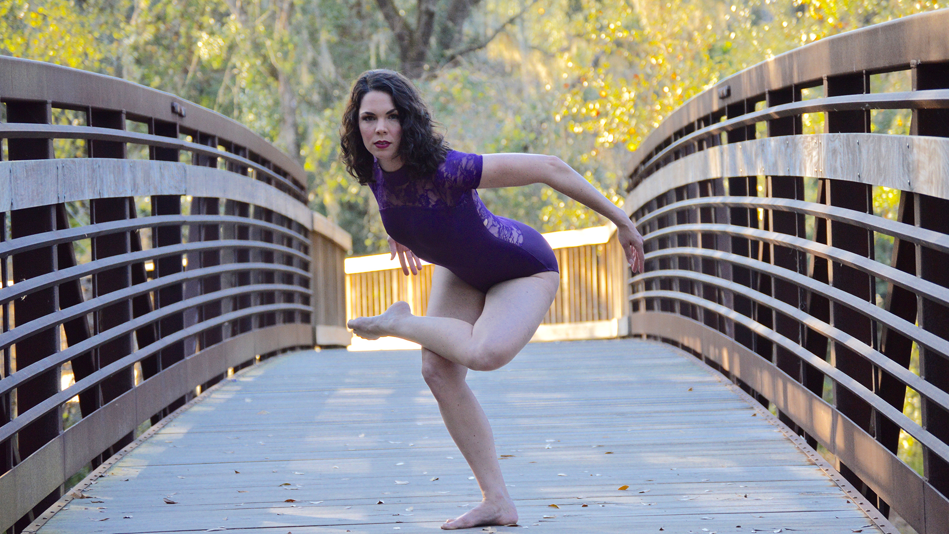 Female dancer in a leotard, posing on one leg outside on a bridge