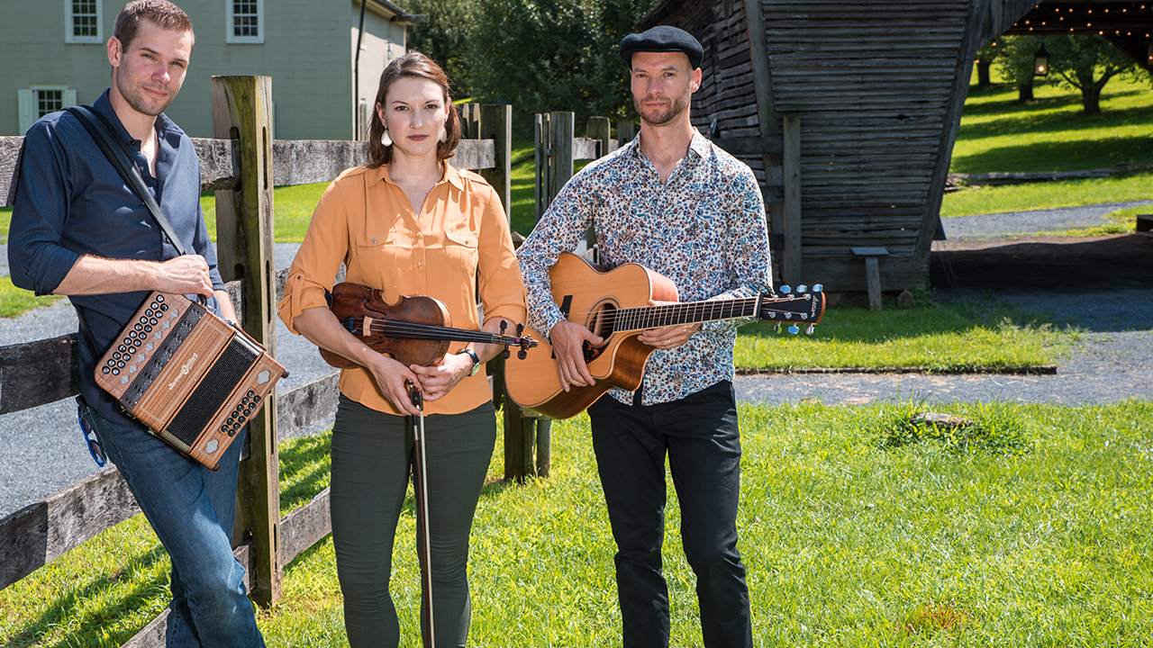 Two male and one female musician posing outside with their instruments in hand