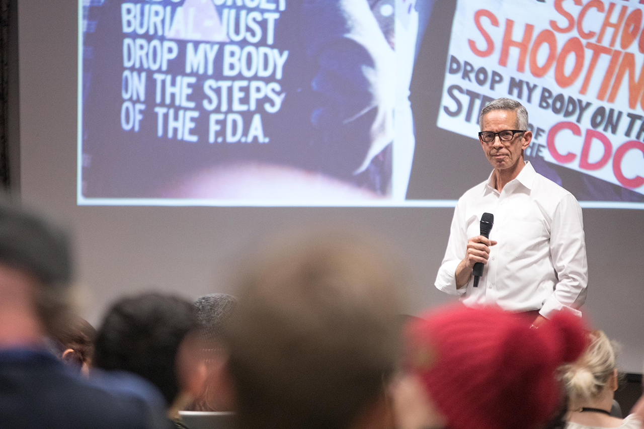 AIDS activist Peter Staley in front of an auditorium of students with a powerpoint displaying images from Act Up