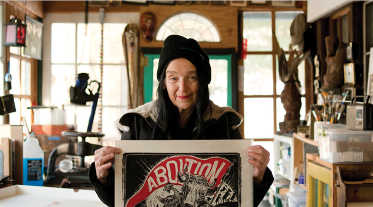 image of Sue Coe in her studio holding up a print 