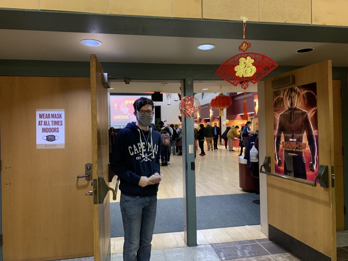 Masked male student walking through the doorway to a large meeting room with lunar New Year decorations 