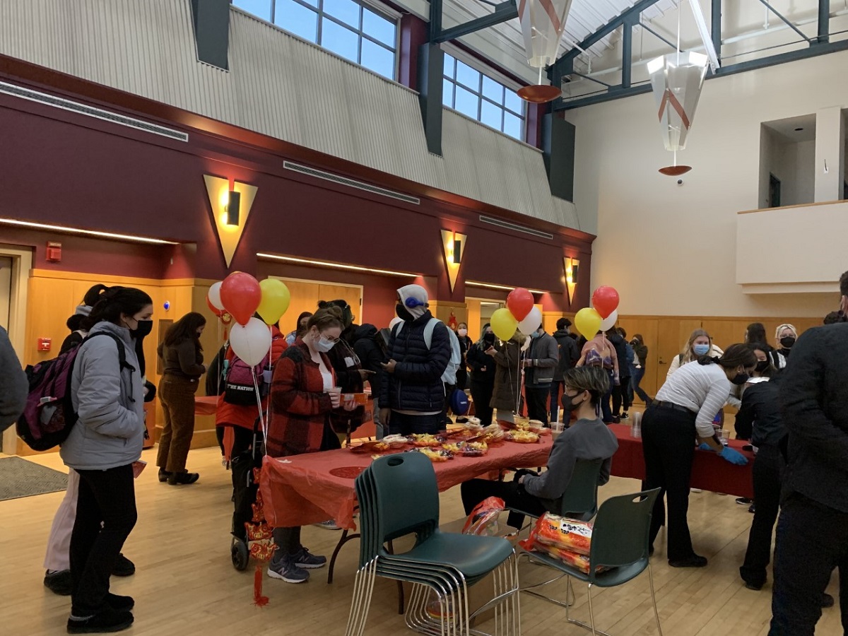 Masked students attend a celebration in the MSU large meeting room, with tables of refreshments and red and yellow balloons around the room 