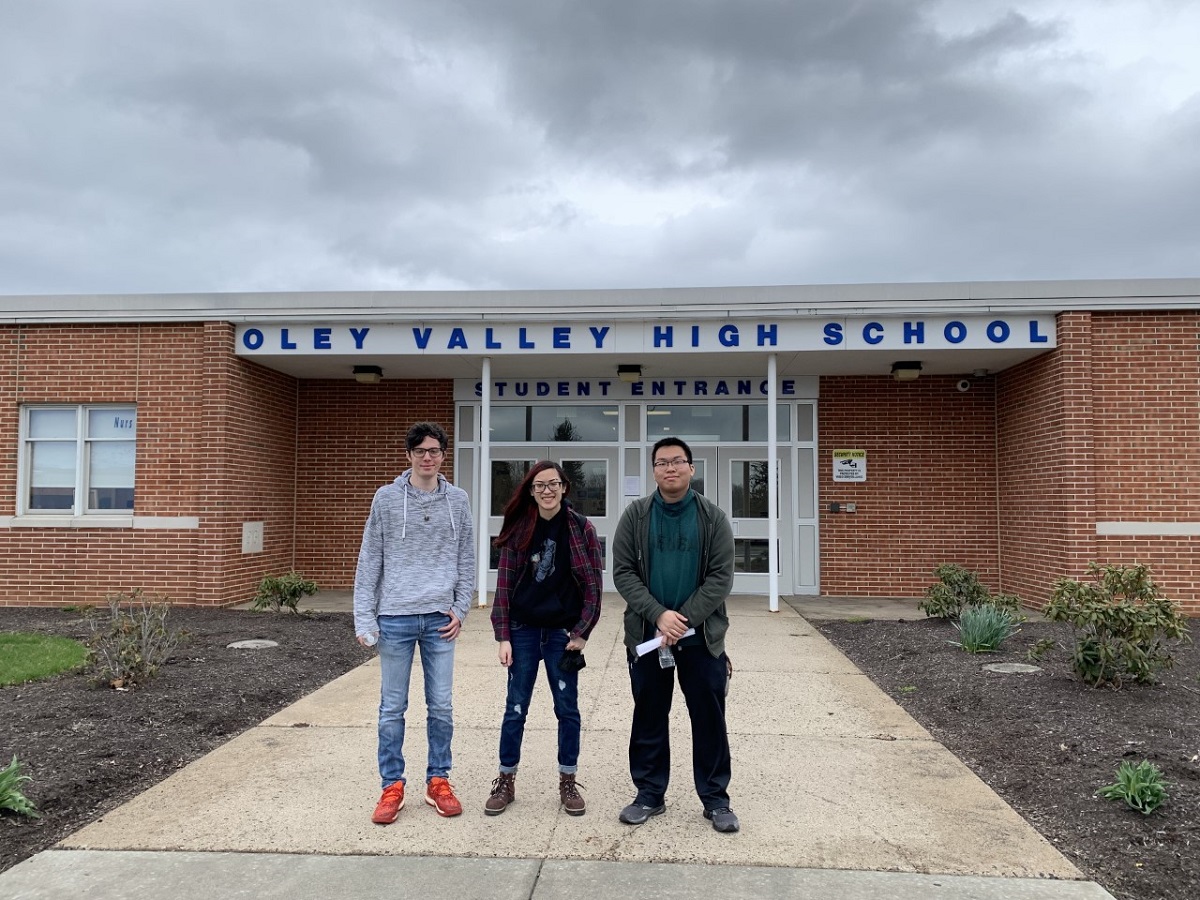 The students smiling outside the front entrance of Oley Valley High School and smiling at the camera  