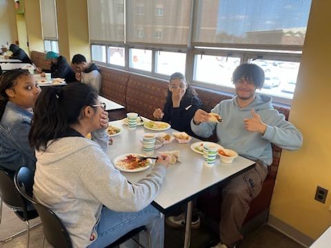 student with group smiling with thumbs up in dining hall