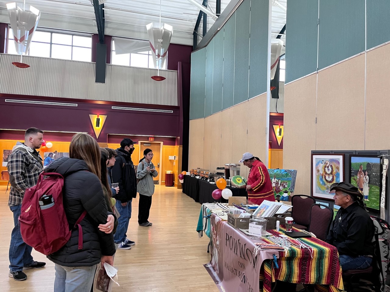 Students watching a man perform with a drum at MCC's Indigenous Showcase indoors.