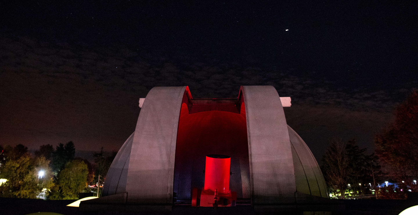 Observatory open at night.  A red light inside the dome reveals the astronomical telescope.