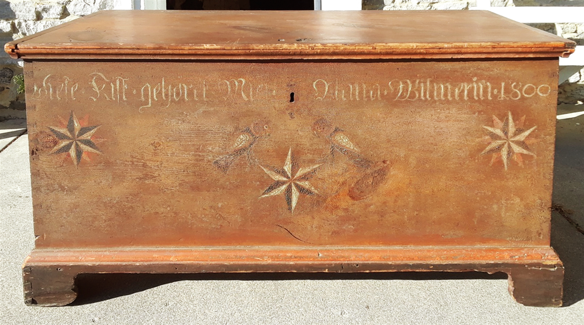 A large brown chest with two parrots, three geometric stars, and German script.