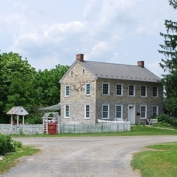 Photo of the front of the stone farmhouse with a white picket garden fence